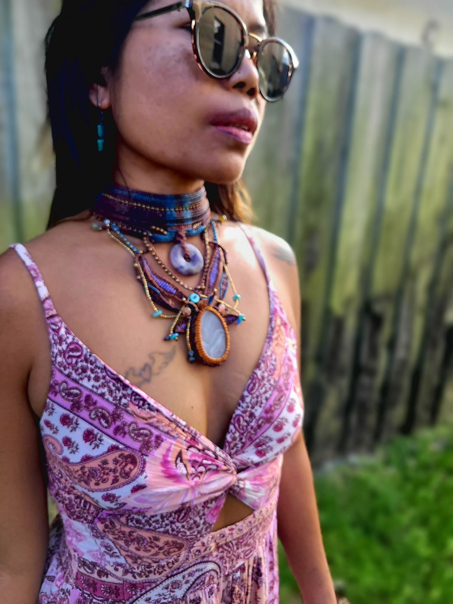 Model wearing ornate woven boho chestplate choker tribal jewelry with sunglasses in a floral dress.