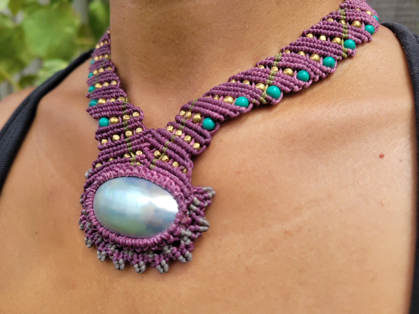 Purple macrame necklace with a large central bead worn by a person.