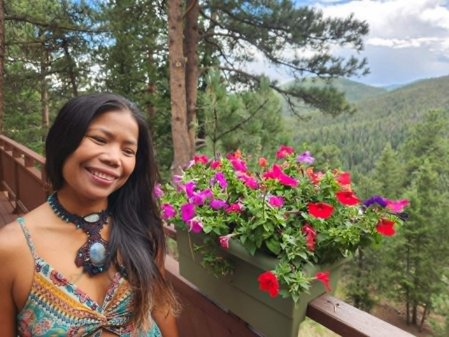 Labradorite Pendant worn by a smiling woman beside vibrant flowers in a scenic mountain setting