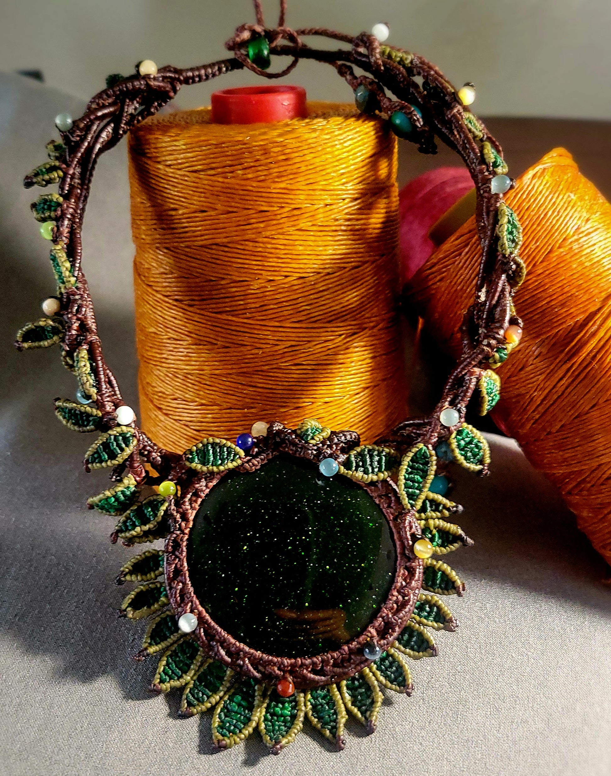 Sandstone Necklace featuring dark green sandstone pendant and micromacramé flower design with leaf motifs.