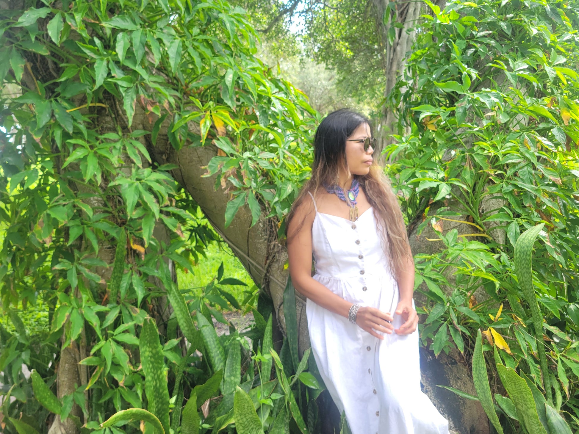 Opal Choker worn by a woman in a white dress standing among lush green foliage.