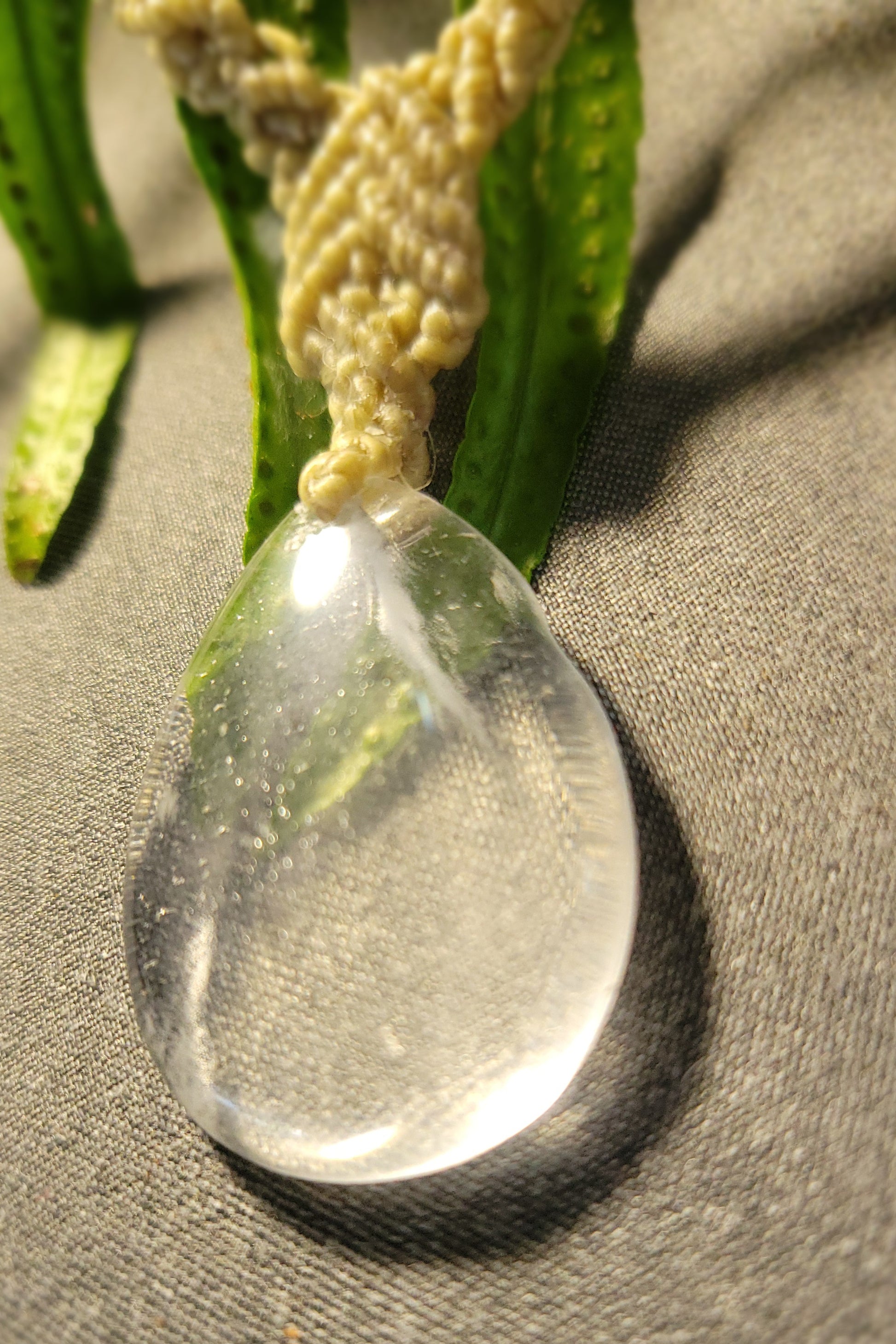 Close-up of Quartz Necklace featuring a natural clear quartz drop pendant and macramé design on a textured surface.