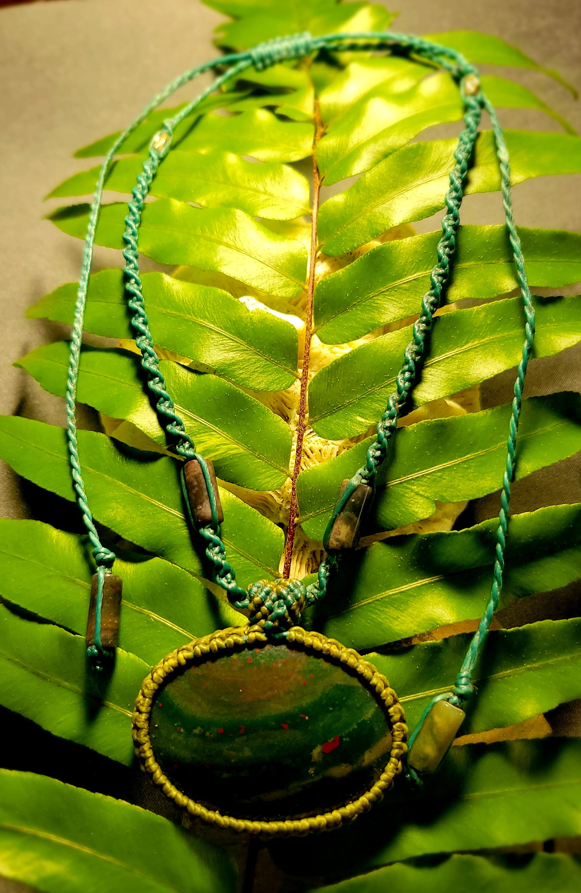 Orbicular Bloodstone Pendant on earthy green leaves, featuring moss agate details and waxed cotton cord.