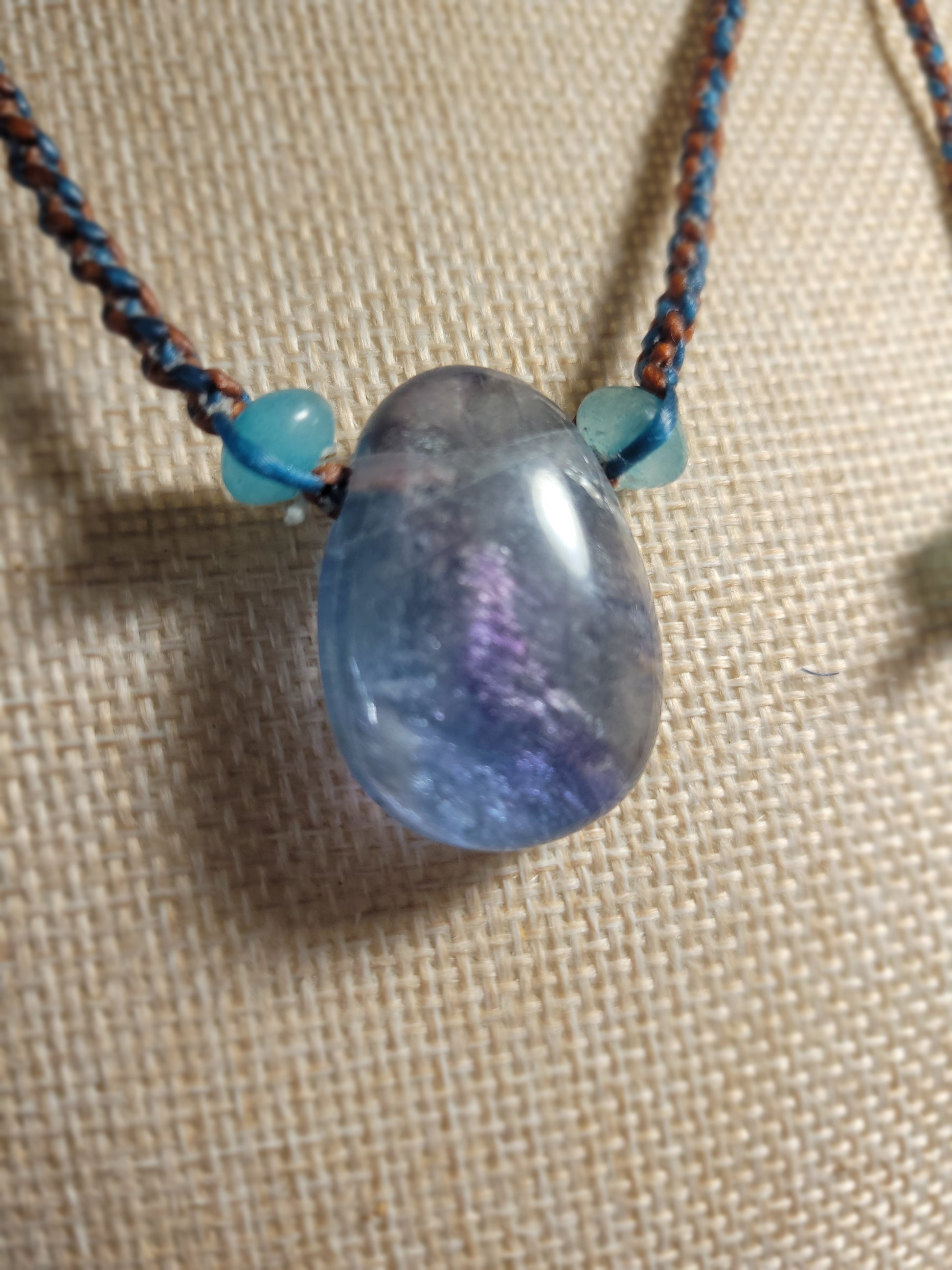 Fluorite Pendant featuring polished fluorite stone with blue beads on a tan spiral-braided cord.