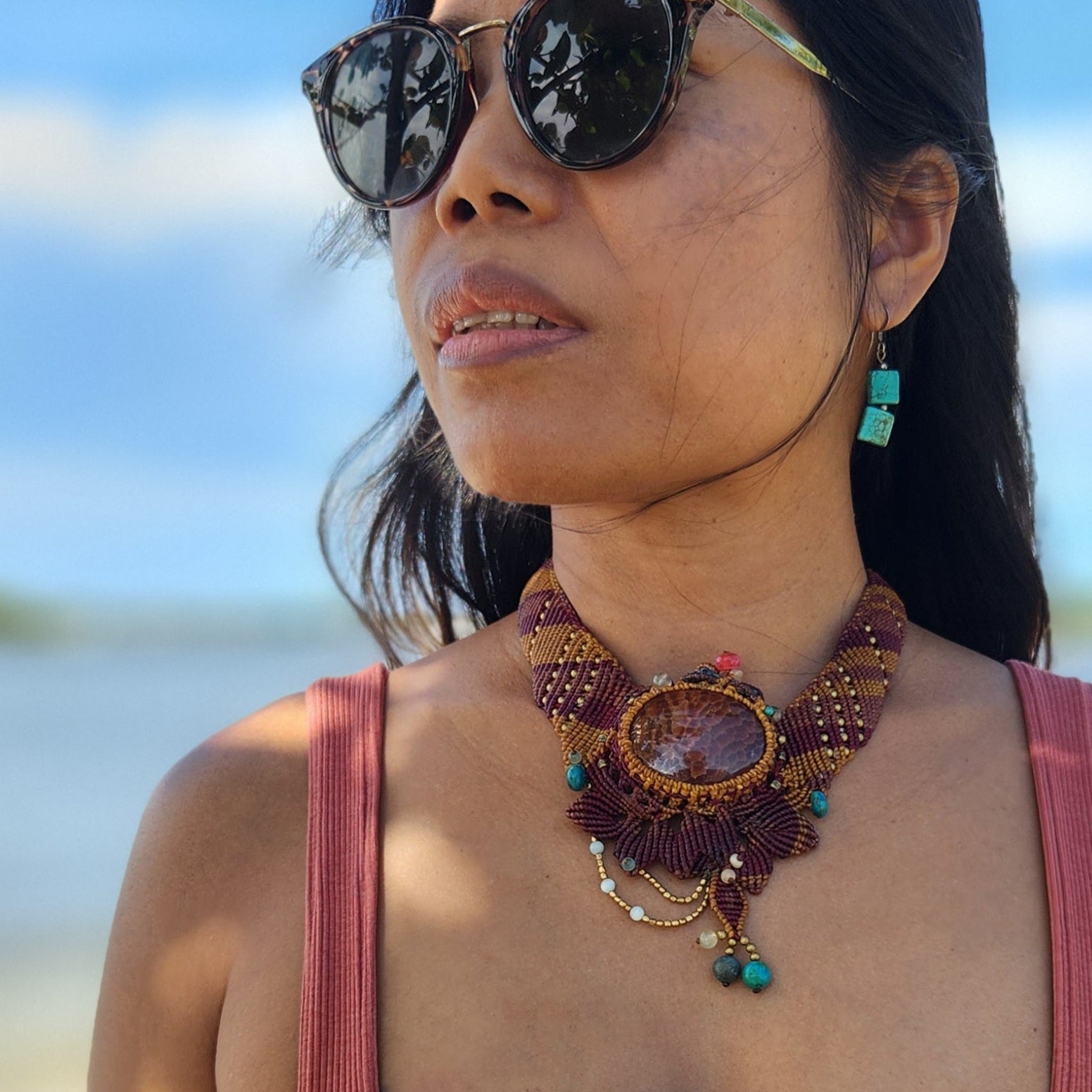 Fire Agate necklace with ornate micromacramé, worn by a woman outdoors with sunglasses.