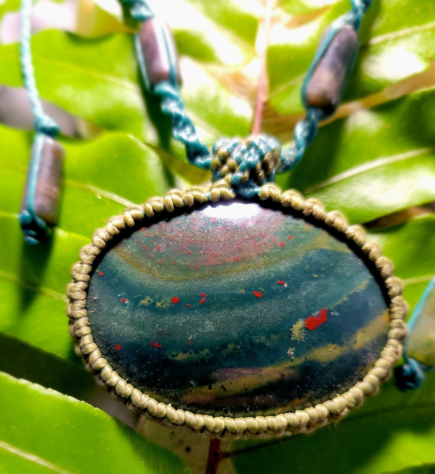 Orbicular Bloodstone Pendant showcasing natural stone with moss agate bead accents and waxed cotton cord, on leaf background.