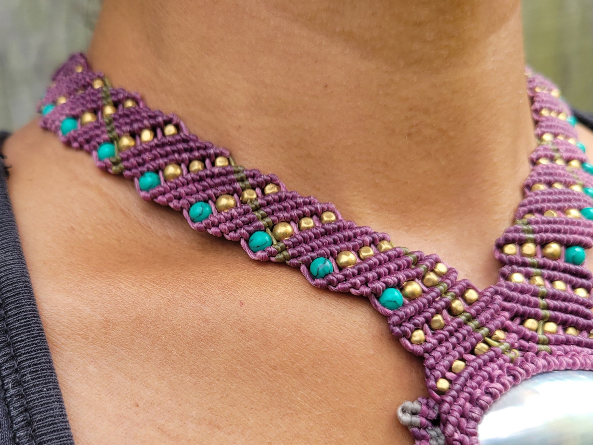 Purple beaded necklace with a large central stone worn by a person against a blurred natural background