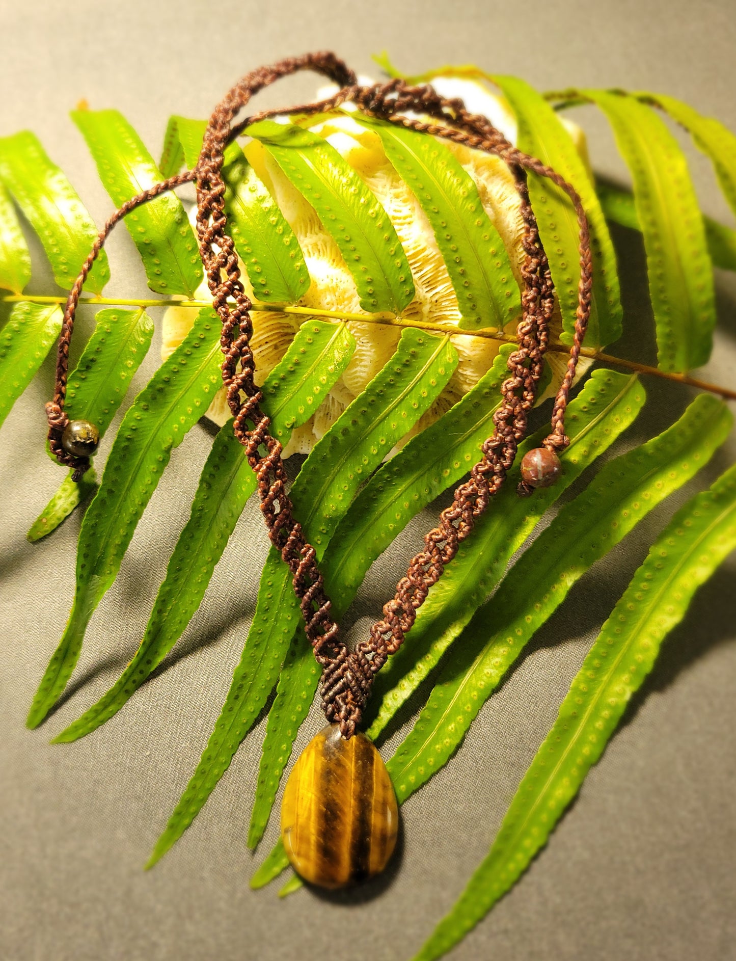 Tiger Eye Necklace – Double Helix Boho Luxe Pendant on a background of green ferns, showcasing natural beauty and elegance.