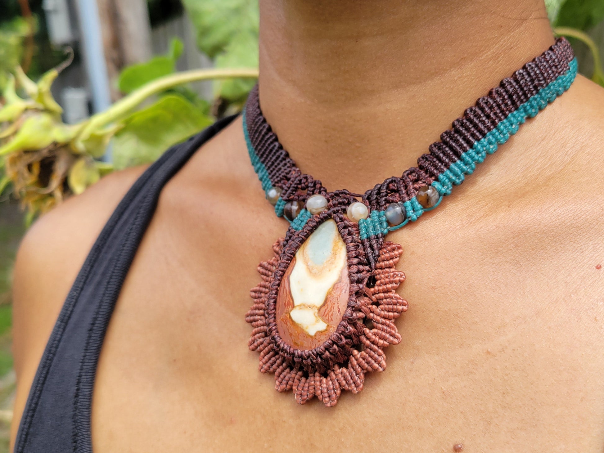 Person wearing a detailed macrame necklace with a large pendant outdoors.