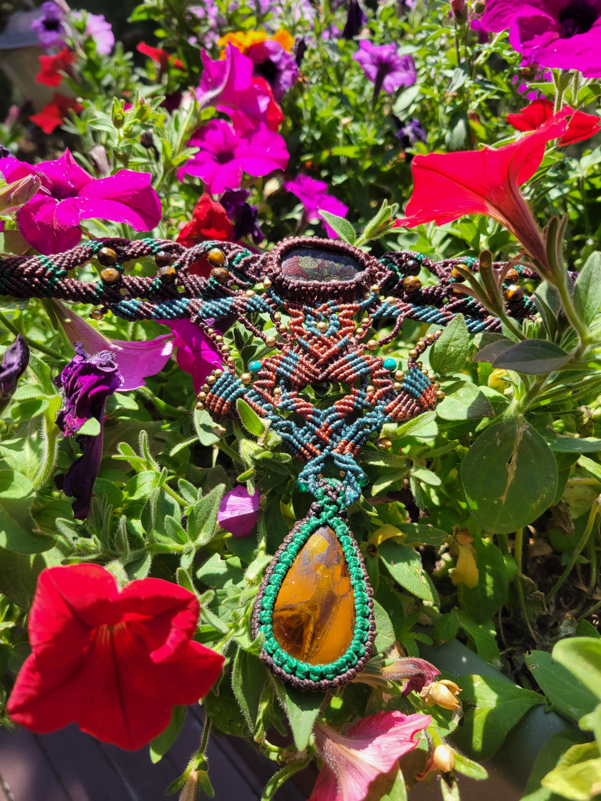 Iron Tiger's Eye Pendant showcasing natural stone and micromacramé design against vibrant flowers.
