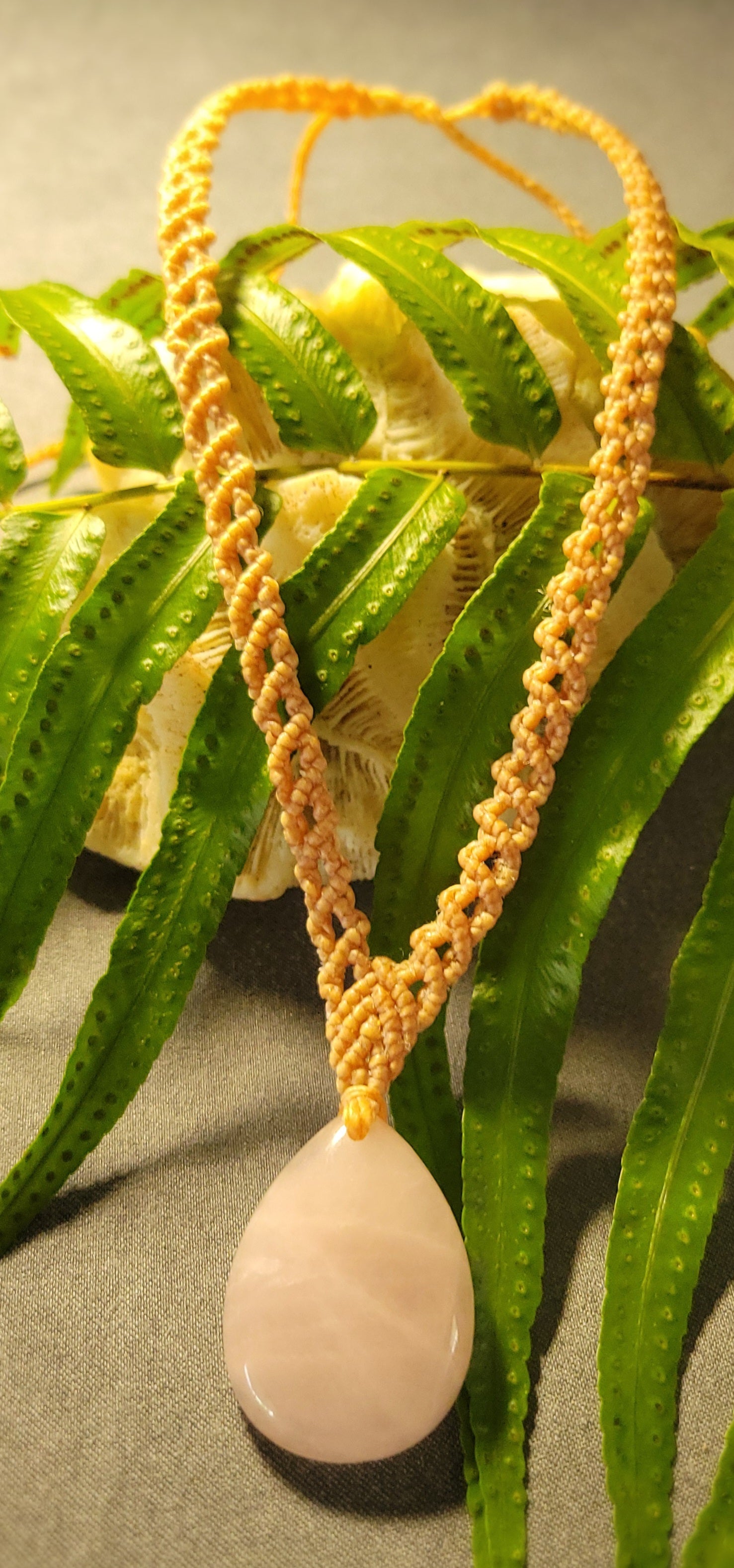 Rose Quartz Pendant on handwoven macramé necklace with light brown cord against green foliage.