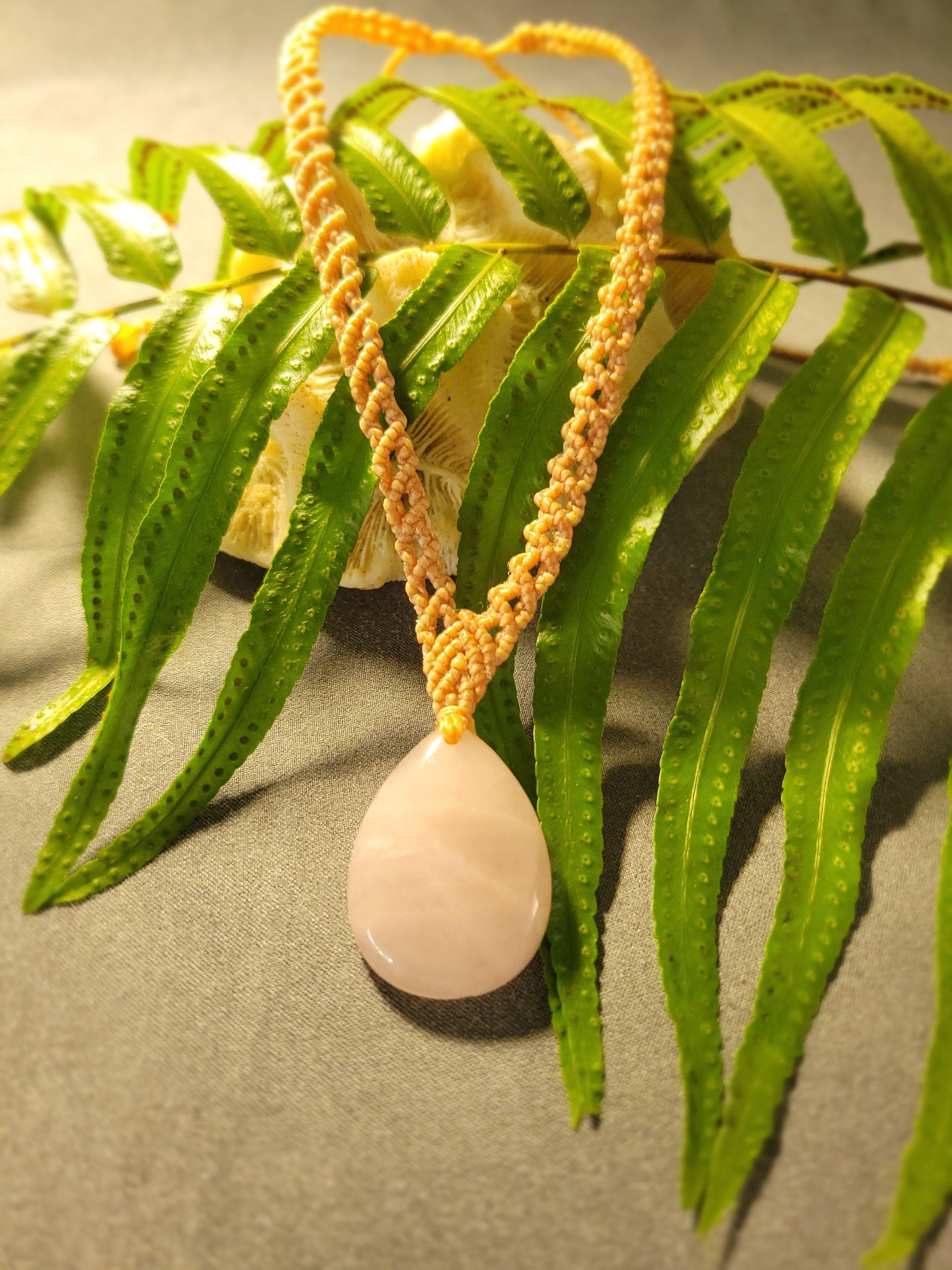 Rose Quartz Pendant – Heart Drop Crystal Macramé Necklace on a fern background with a beige cord.