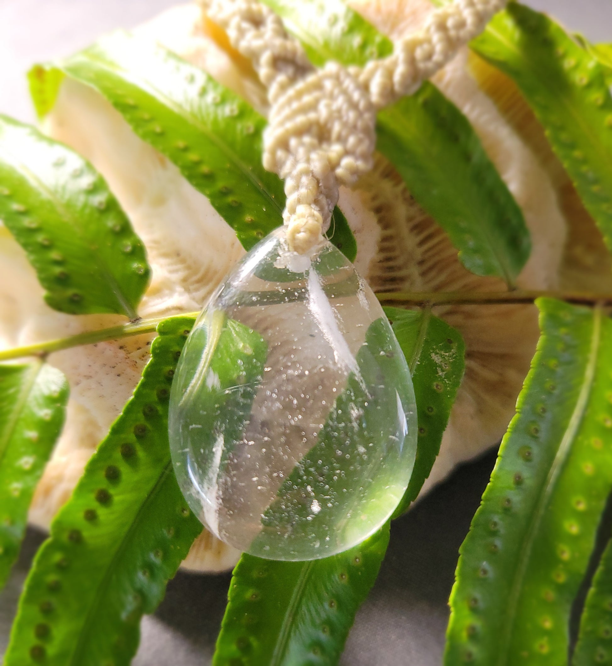 Quartz Necklace featuring a drop crystal pendant with macramé design on green fern leaves.