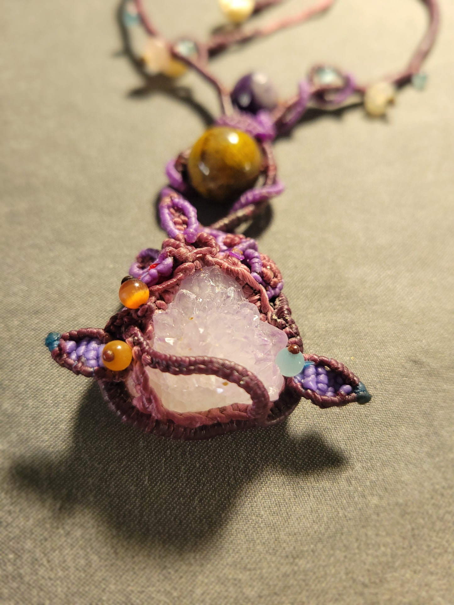 Amethyst Crystal Necklace featuring a large raw amethyst pendant and woven macramé details with earthy tones.