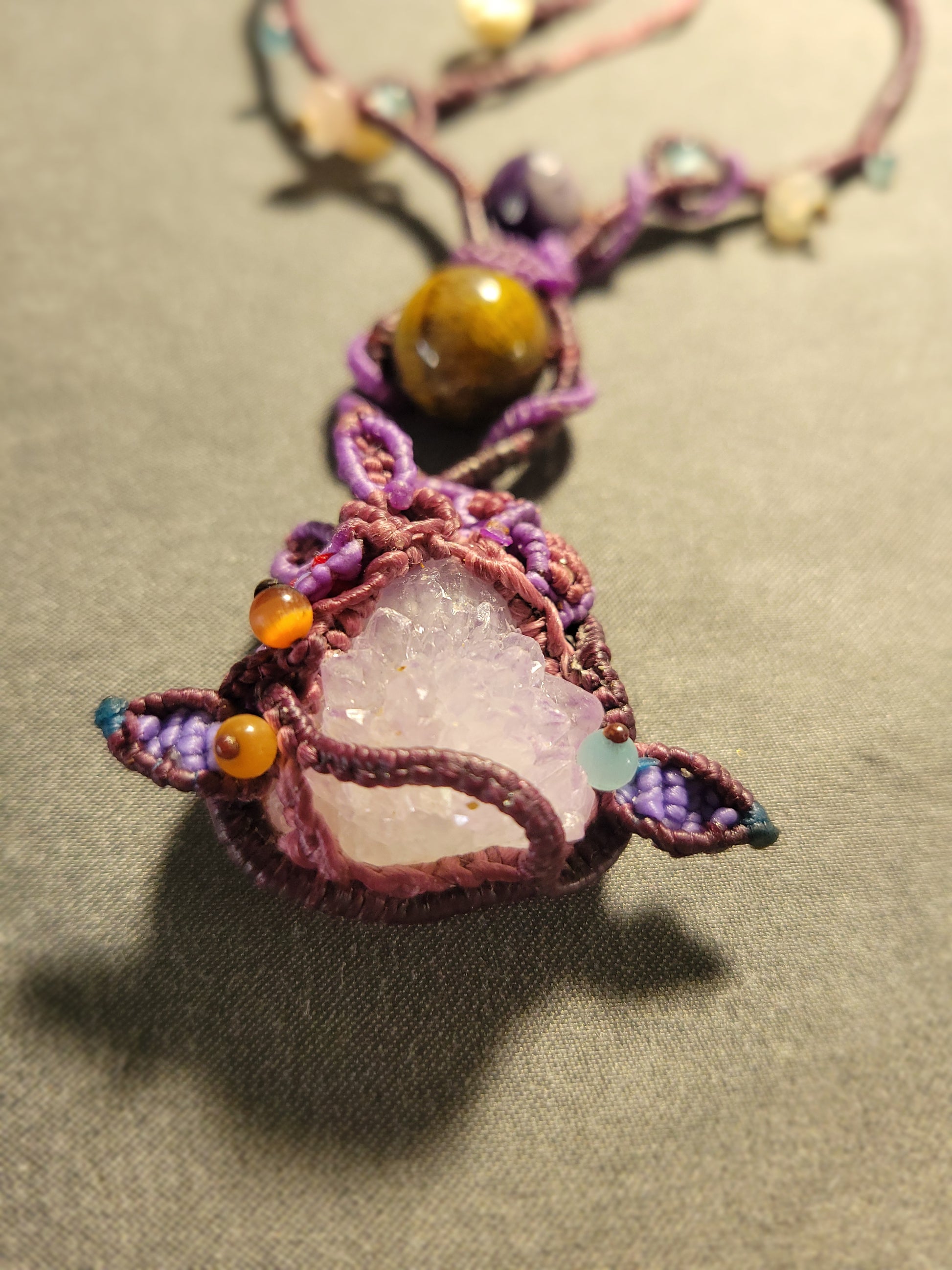 Amethyst Crystal Necklace featuring a large raw amethyst pendant and woven macramé details with earthy tones.