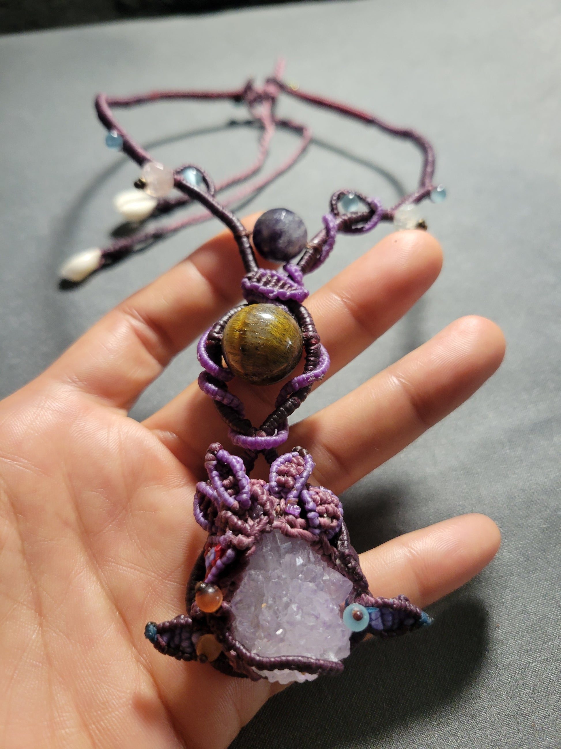 Amethyst Crystal Necklace featuring a raw amethyst pendant and tiger eye stone, displayed in a hand.